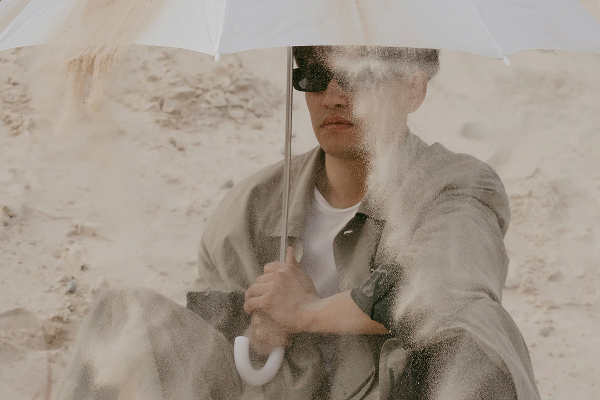 Sand Pouring on the Man in Gray Long Sleeves Holding White Umbrella